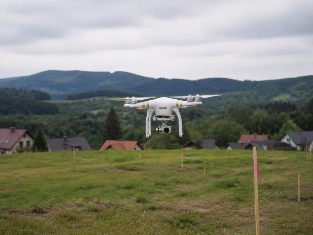 Dron pomiarowy unoszący się nad zieloną działką budowlaną